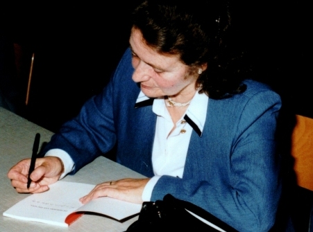 Foto van de auteur zittend aan een tafel terwijl ze een boek signeert