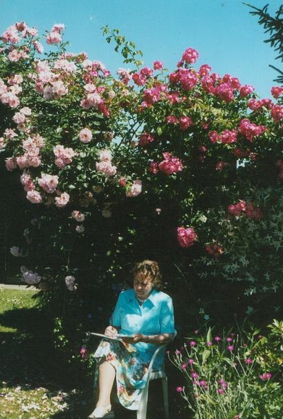 Foto van de auteur onder de pergola vol met licht- en donker-roze rozen